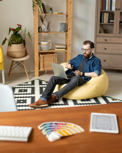 Young male freelance designer sitting in comfortable armchair in front of his workplace and drawing sketches of new logo with stylus at home